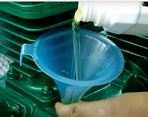 New compressor oil slowly pouring into a funnel placed at the compressor’s oil filling port during routine maintenance.