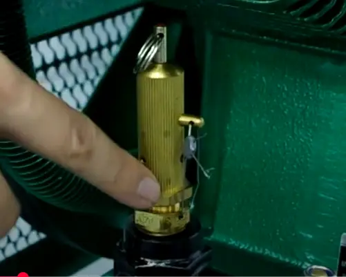 Technician placing his finger near the connection of an air compressor safety valve to detect any air leaks after maintenance.