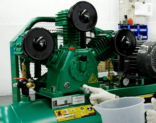 Technician placing a drain pan under the oil drain plug of an air compressor to catch used oil.