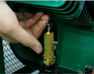 Technician pulling the ring of an air compressor safety valve with his finger to test it after service and ensure it releases air properly.