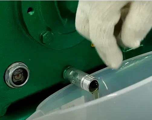 Used oil flowing from the drain plug of an air compressor into a drain pan during routine servicing.